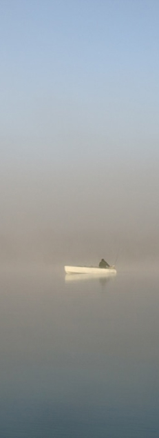 a lone fisherman on a foggy lake early in the morning